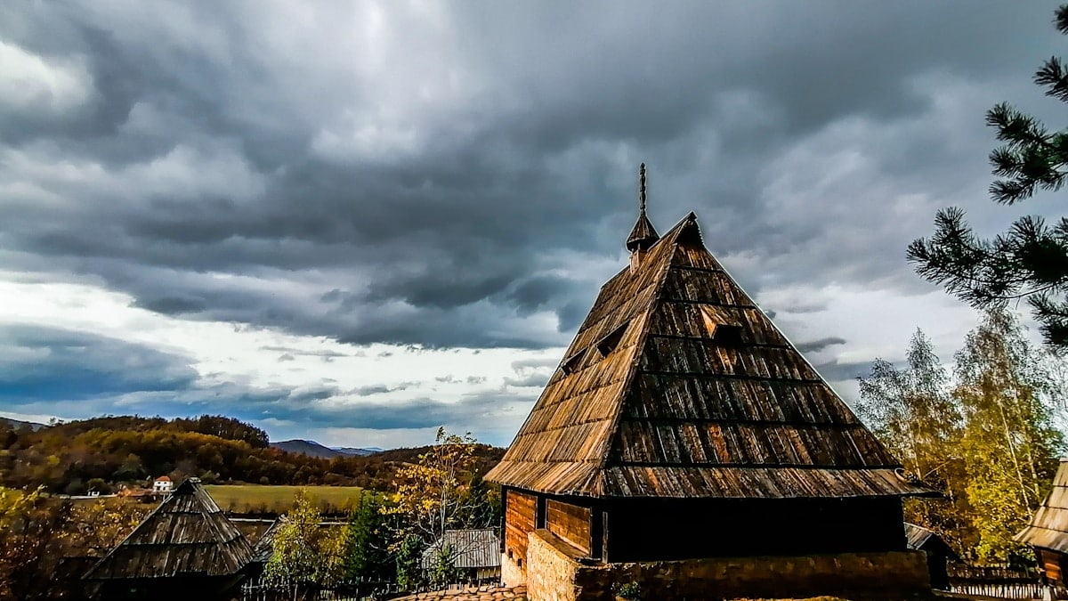 brown wooden house on green grass field under gray clouds